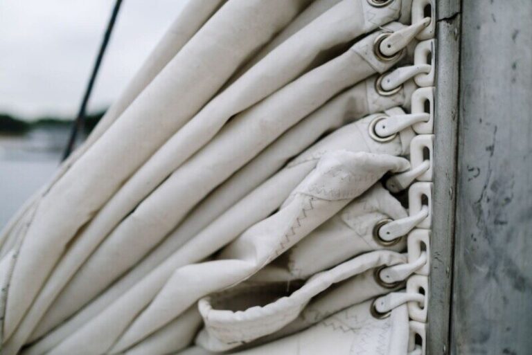 Detailed view of a folded sail secured with metal rings against a boat mast.