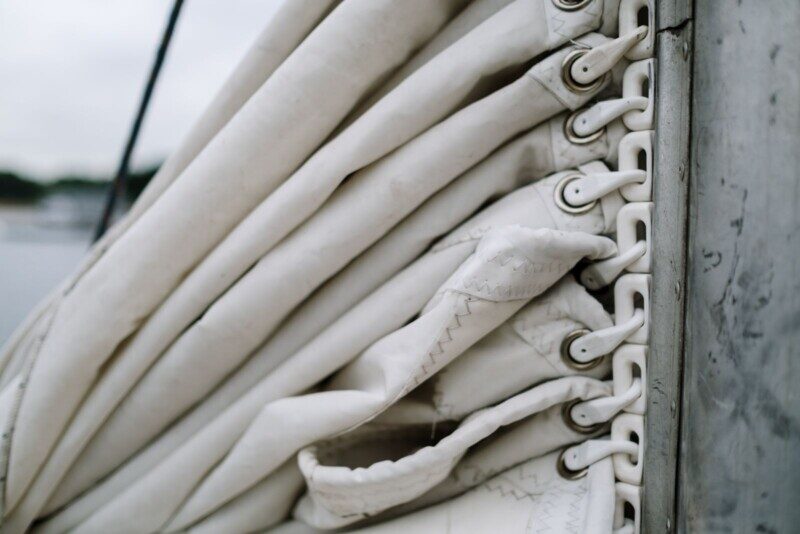 Detailed view of a folded sail secured with metal rings against a boat mast.